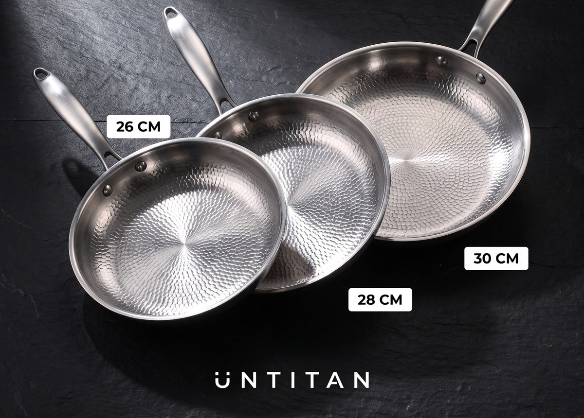 Trois poêles à surface de cuisson en titane de 26, 28 et 30 cm posées sur une ardoise
