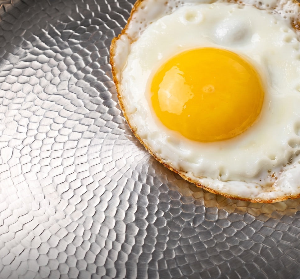Œuf au plat qui cuit sur une surface de cuisson en titane martelée
